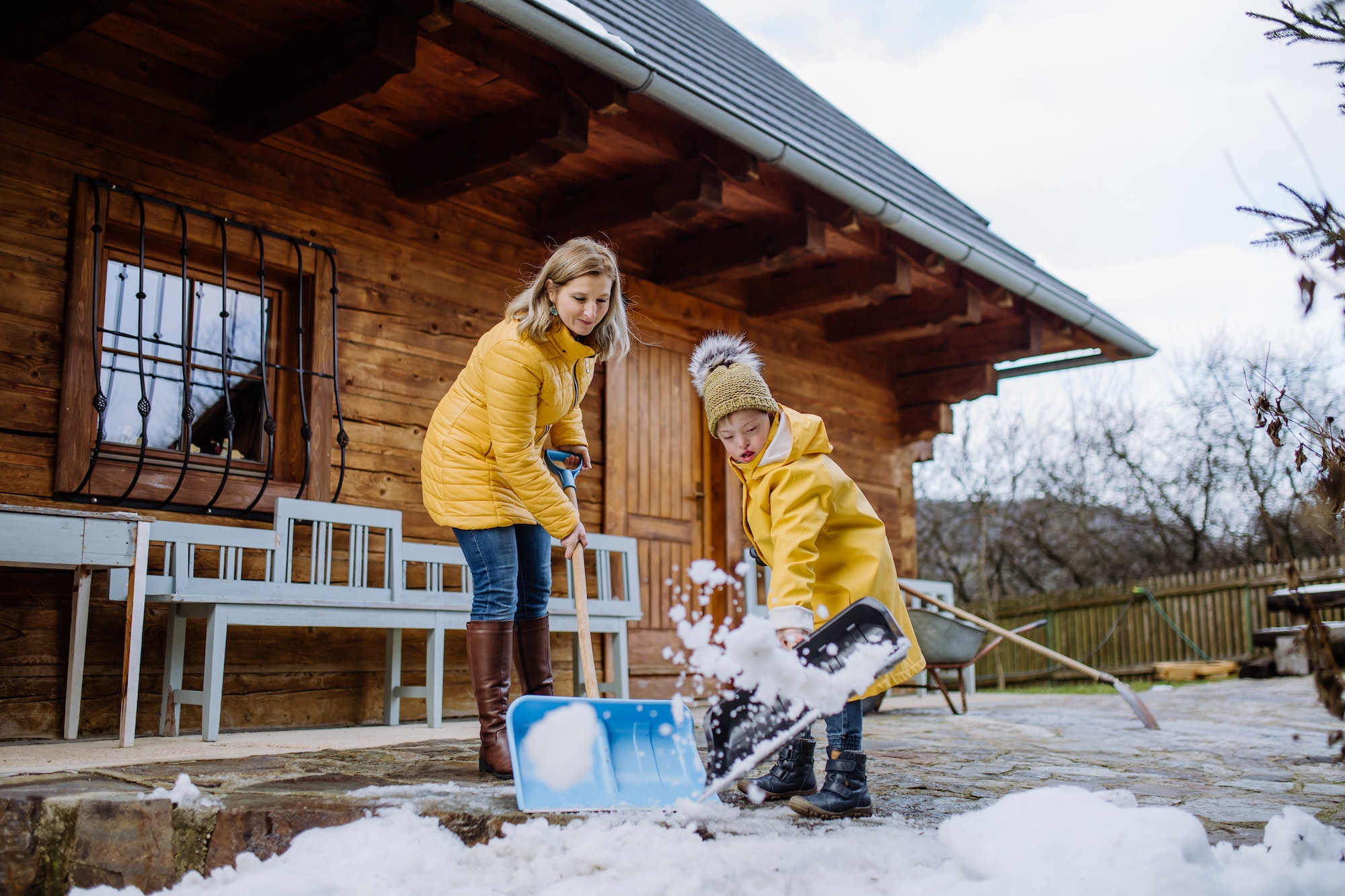 Boy with Down syndrome with his mother clearing snow from path with shovel in front of house